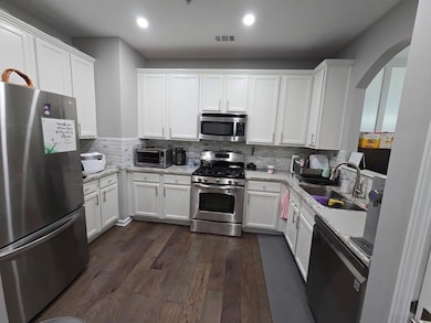 Kitchen with stainless steel appliances, a sink, arched walkways, white cabinets, and dark wood-style floors