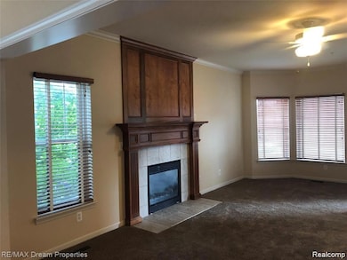 Unfurnished living room featuring ornamental molding, a fireplace, carpet, and a ceiling fan