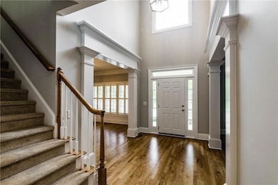 Foyer entrance featuring plenty of natural light, a towering ceiling, ornate columns, wood finished floors, and stairway
