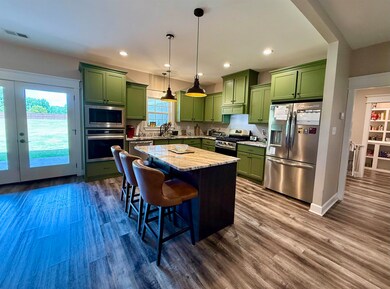Kitchen with green cabinets, appliances with stainless steel finishes, dark wood-style floors, and recessed lighting