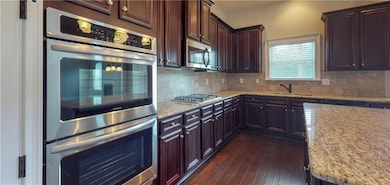 Stock photo of kitchen featuring appliances with stainless steel finishes, a sink, backsplash, dark wood-style flooring, and light stone counters