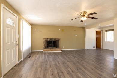 Unfurnished living room with a ceiling fan, wood finished floors, a brick fireplace, and a textured ceiling