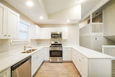 Kitchen featuring appliances with stainless steel finishes, a sink, a peninsula, white cabinets, and vaulted ceiling