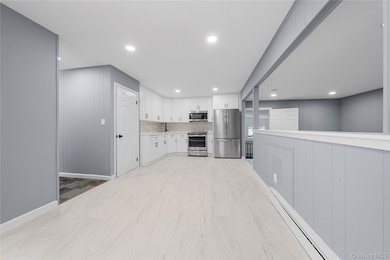 Kitchen featuring stainless steel appliances, light countertops, white cabinets, a baseboard radiator, and backsplash