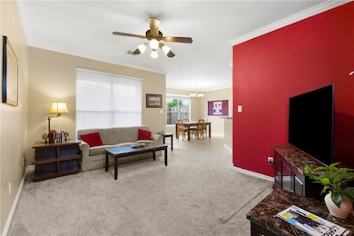 Living area with ornamental molding, light colored carpet, a ceiling fan, and a chandelier