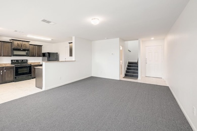 Kitchen with black appliances, dark brown cabinetry, light colored carpet, open floor plan, and a peninsula