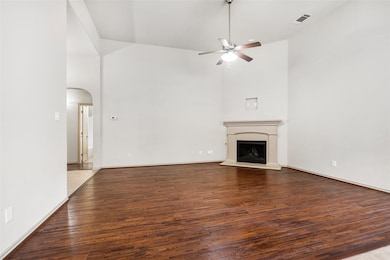 Unfurnished living room with arched walkways, wood finished floors, a fireplace with raised hearth, high vaulted ceiling, and ceiling fan
