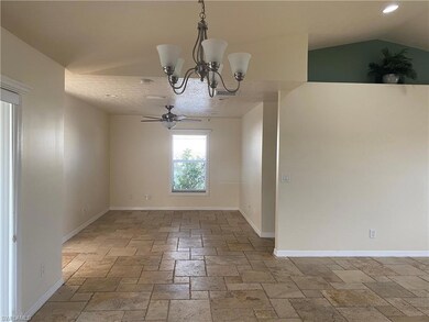 Unfurnished room with stone tile flooring, a chandelier, a ceiling fan, lofted ceiling, and baseboards