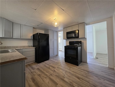 Kitchen with black appliances, a drop ceiling, light countertops, light wood finished floors, and gray cabinetry