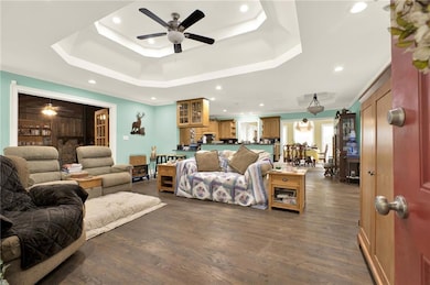 Living area with a ceiling fan, a raised ceiling, dark wood-style floors, and recessed lighting