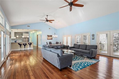 Living area with french doors, a ceiling fan, high vaulted ceiling, hardwood / wood-style floors, and a chandelier
