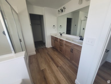 Bathroom with a shower stall, double vanity, dark wood-style floors, and a walk in closet