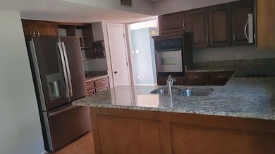 Kitchen featuring light stone countertops, appliances with stainless steel finishes, a peninsula, open shelves, and light wood-style floors
