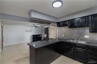 Kitchen featuring dark cabinetry, a peninsula, a ceiling fan, and tasteful backsplash
