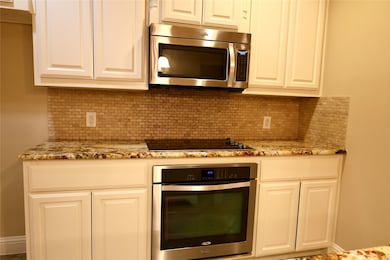 Kitchen with stainless steel appliances, tasteful backsplash, light stone countertops, and white cabinetry