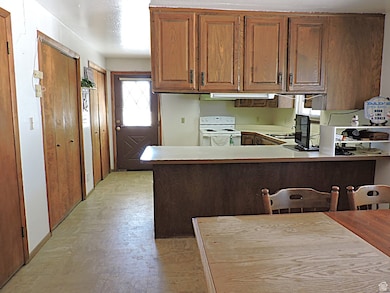 Kitchen featuring light countertops, a peninsula, white electric stove, and brown cabinetry