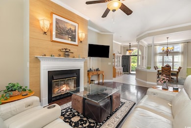 Living room featuring a chandelier, ceiling fan, ornamental molding, a glass covered fireplace, and wood finished floors