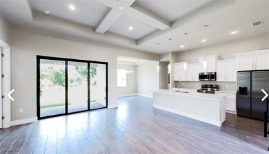 Kitchen with refrigerator with ice dispenser, pendant lighting, white cabinets, beamed ceiling, and an island with sink