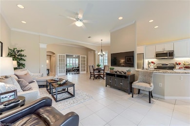 Living room featuring arched walkways, a ceiling fan, a chandelier, light tile patterned floors, and ornamental molding