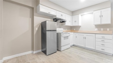 Kitchen with freestanding refrigerator, white electric stove, light countertops, and white cabinets