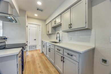 Kitchen with stainless steel electric range oven, extractor fan, decorative backsplash, light hardwood / wood-style flooring, and sink