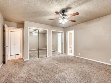 Unfurnished bedroom featuring a textured ceiling, light colored carpet, ceiling fan, and two closets