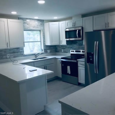Kitchen with appliances with stainless steel finishes, backsplash, white cabinetry, a peninsula, and recessed lighting
