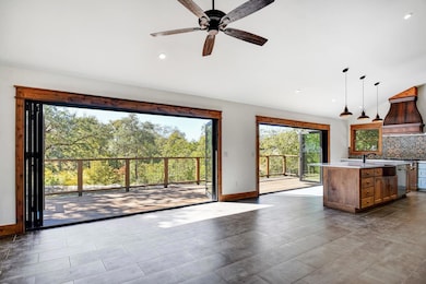 Kitchen featuring decorative backsplash, pendant lighting, an island with sink, premium range hood, and ceiling fan