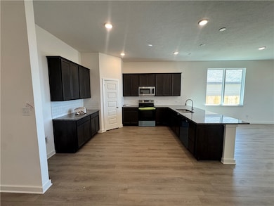 Kitchen with backsplash, appliances with stainless steel finishes, a peninsula, light stone countertops, and recessed lighting
