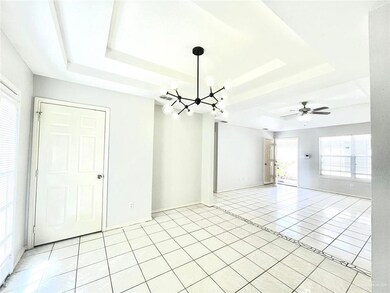 Tiled spare room featuring ceiling fan with notable chandelier and a raised ceiling