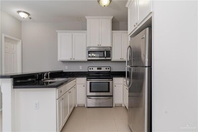 Kitchen with stainless steel appliances, a peninsula, white cabinets, light tile patterned floors, and a sink