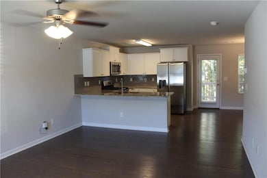 Kitchen featuring decorative backsplash, stainless steel appliances, white cabinetry, a peninsula, and dark wood-style flooring