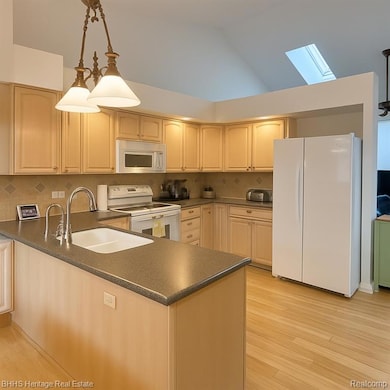 Kitchen with white appliances, hanging light fixtures, a skylight, light wood finished floors, and lofted ceiling