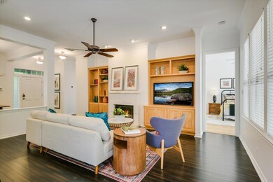Living area with ornamental molding, dark wood-type flooring, a tiled fireplace, ceiling fan, and recessed lighting