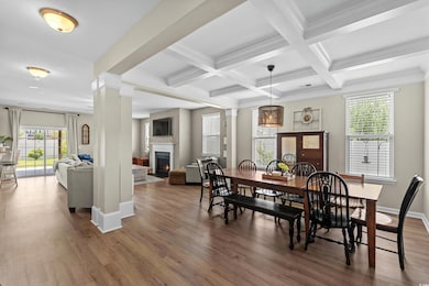 Dining space featuring beamed ceiling, a lit fireplace, ornate columns, wood finished floors, and baseboards