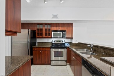 Kitchen with light tile patterned floors, stainless steel appliances, sink, and dark stone countertops