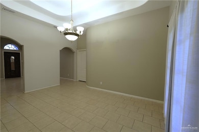 Empty room with a chandelier, light tile patterned floors, arched walkways, and a high ceiling