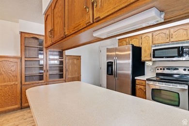 Kitchen with appliances with stainless steel finishes, light countertops, light wood finished floors, and glass insert cabinets