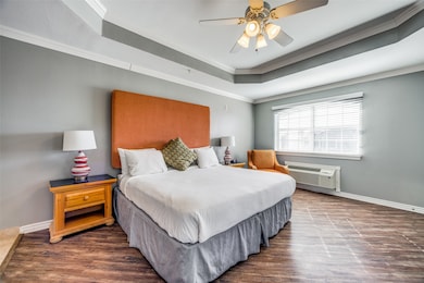 Bedroom featuring dark hardwood / wood-style floors, a wall unit AC, a raised ceiling, ceiling fan, and crown molding