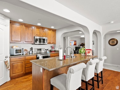 Kitchen with light stone counters, light wood-type flooring, a breakfast bar area, arched walkways, and recessed lighting