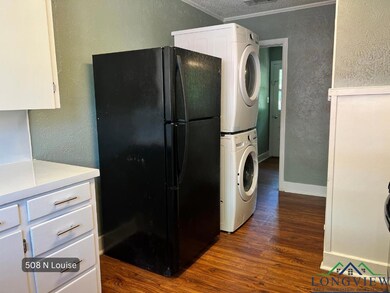 Kitchen featuring freestanding refrigerator, stacked washer and clothes dryer, a textured wall, dark wood-type flooring, and white cabinets