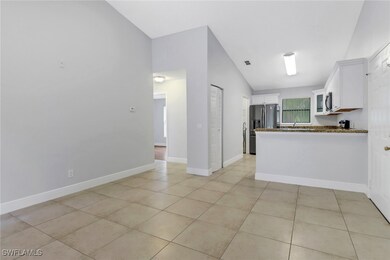 Kitchen featuring vaulted ceiling, kitchen peninsula, light tile patterned floors, white cabinetry, and appliances with stainless steel finishes