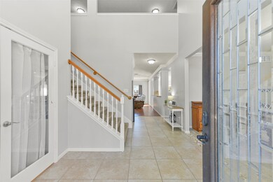 A solid mahogany and leaded glass west-facing front door opens from the covered front porch into a grand foyer with a soaring two-story ceiling, a beautiful chandelier, tile floors, neutral paint, and views all the way to the rear of the home.