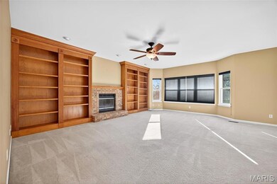 Unfurnished living room featuring built in shelves, a brick fireplace, light colored carpet, and a ceiling fan