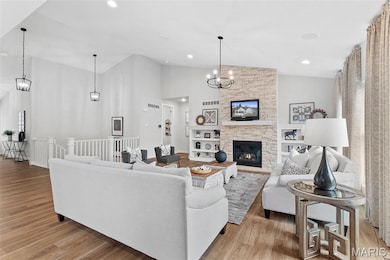 Living area featuring light wood-style flooring, a chandelier, high vaulted ceiling, a stone fireplace, and recessed lighting