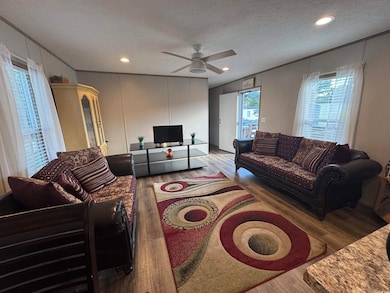 Living area featuring wood finished floors, ornamental molding, a textured ceiling, a ceiling fan, and a decorative wall
