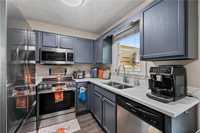 Kitchen featuring stainless steel appliances, a textured ceiling, dark wood finished floors, gray cabinets, and light stone counters