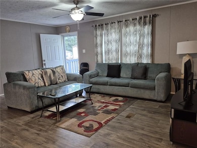 Living room featuring a textured ceiling, dark wood-type flooring, crown molding, a decorative wall, and a ceiling fan