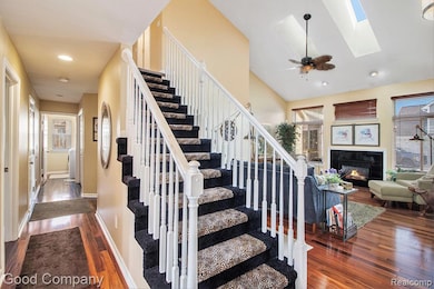 Staircase with hardwood / wood-style floors, a glass covered fireplace, recessed lighting, a skylight, and ceiling fan