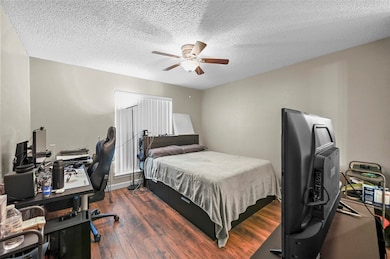 Bedroom with a desk, dark wood-style floors, a textured ceiling, and a ceiling fan